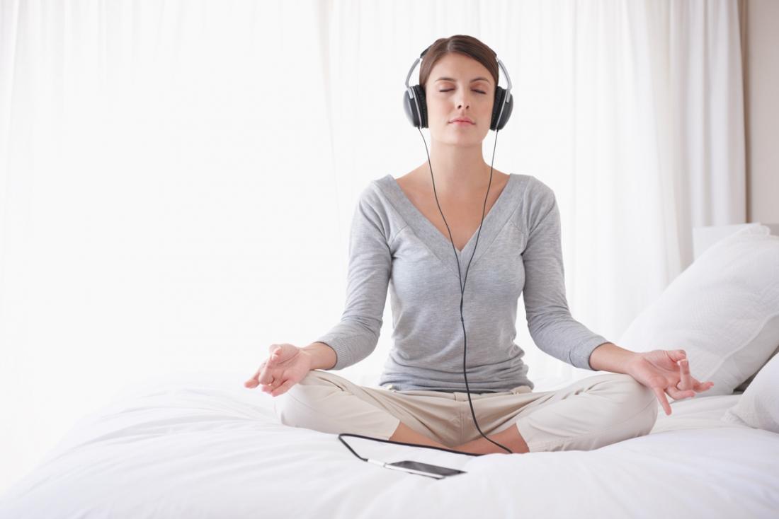 Woman sitting cross legged in lotus yoga position, meditating while listening to headphones.