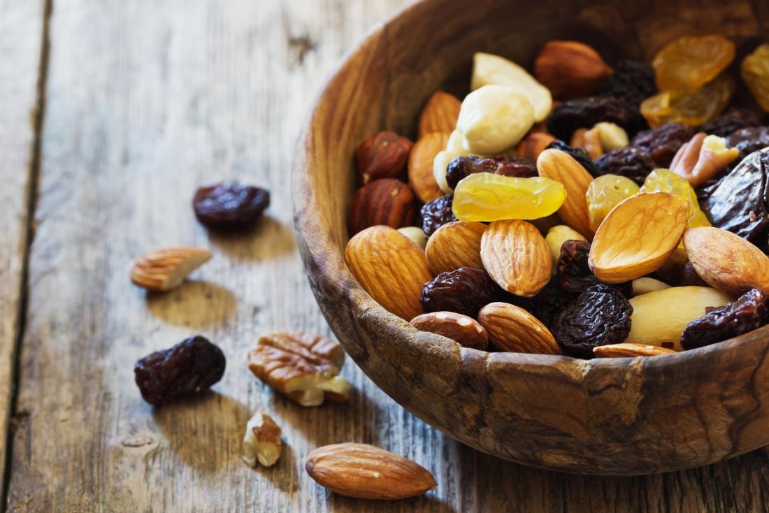 Dried fruits and nuts in a wooden bowl, including raisins, sultanas, almonds, and hazelnuts.