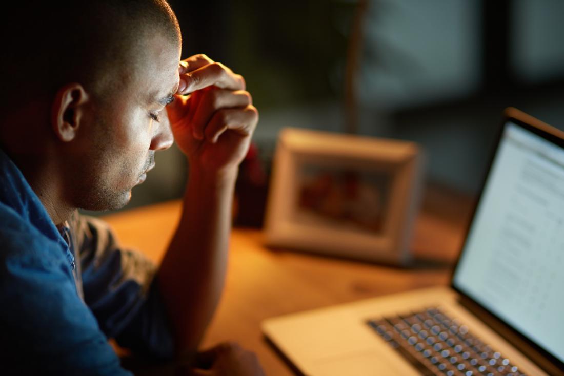 Stressed man with headache in front of laptop.