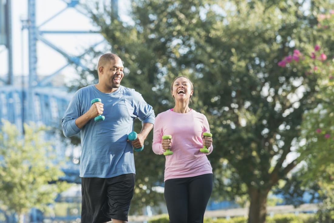 Couple power walking outside and holding hand weights.