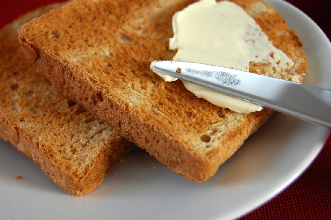 toast on a plate, being buttered with spread.