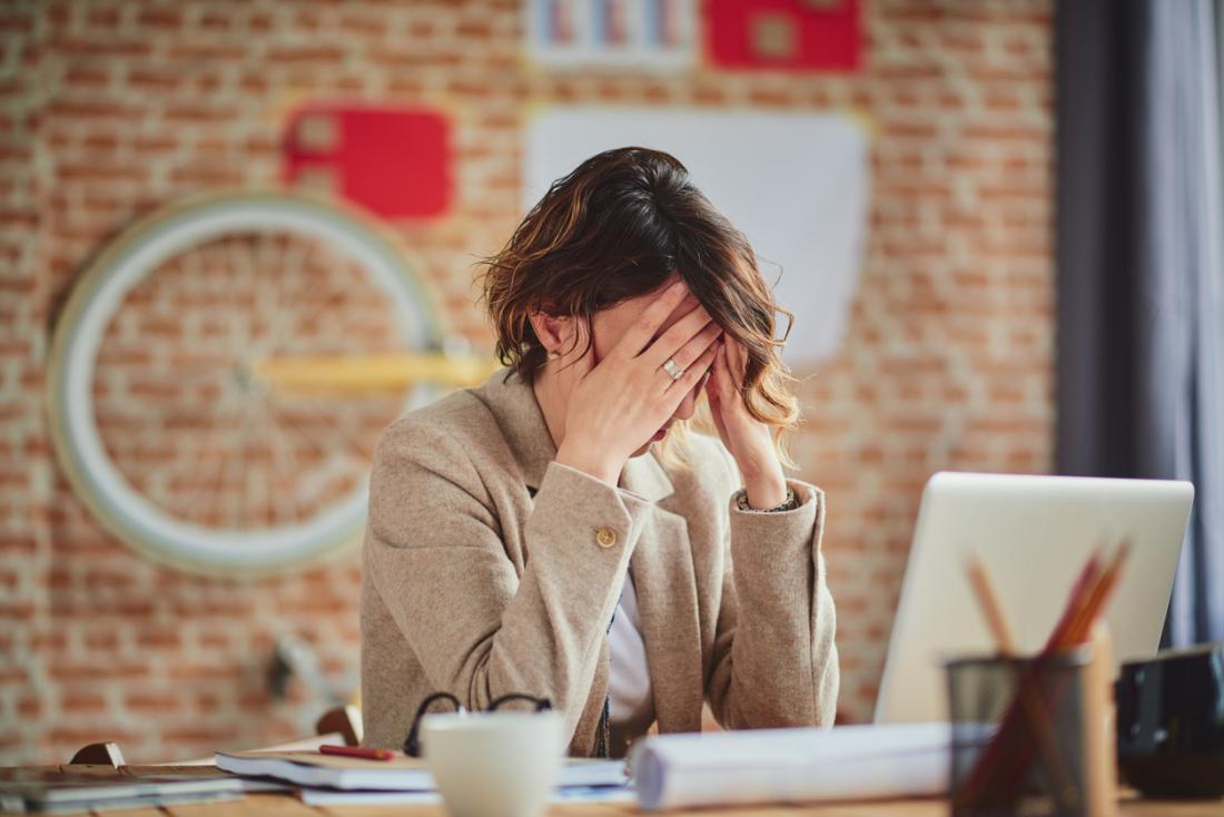 stressed and anxious woman at work, tired and rubbing her temples because of a headache.