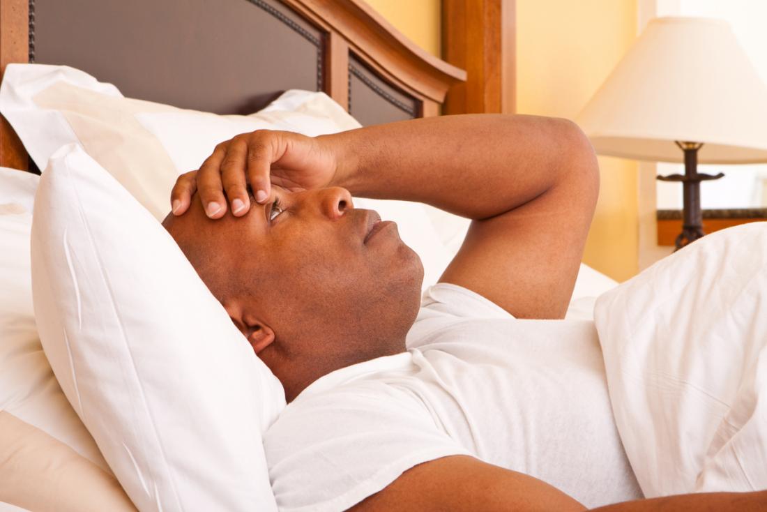 Man suffering from insomnia and poor sleep, laying awake in bed.