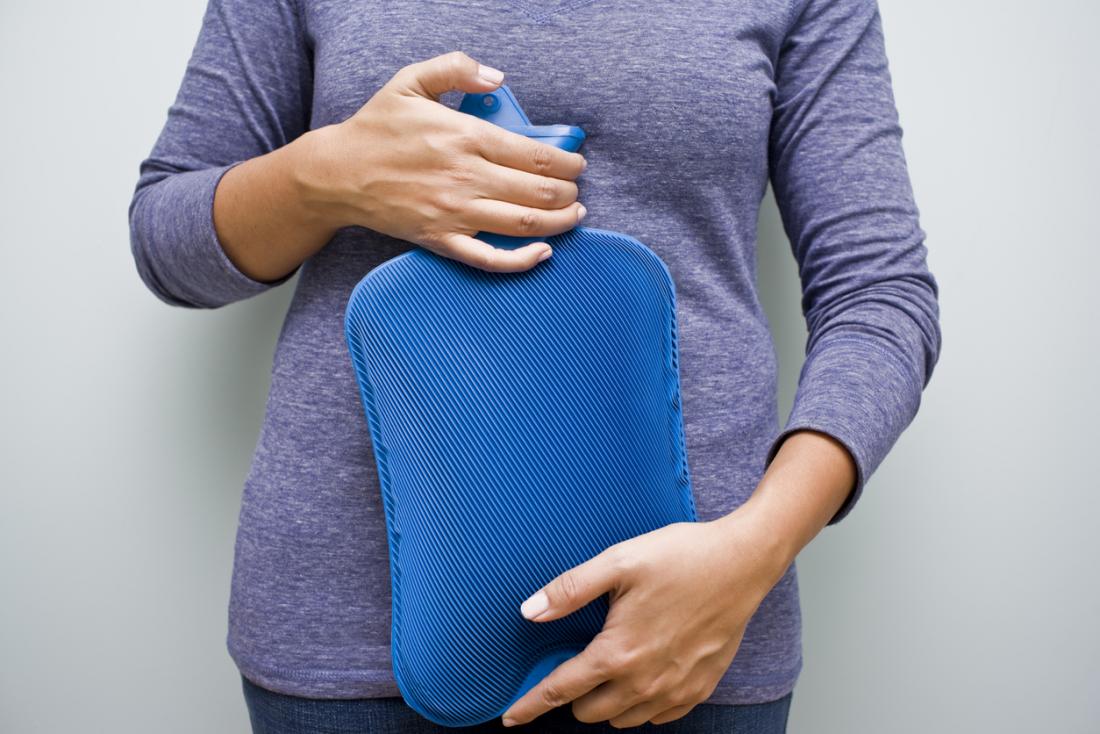 Woman holding a hot water bottle to her abdomen.