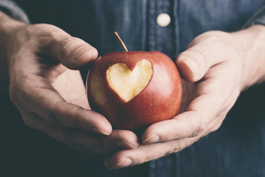 Apple being held in man's hands with heart shape cut out of it.