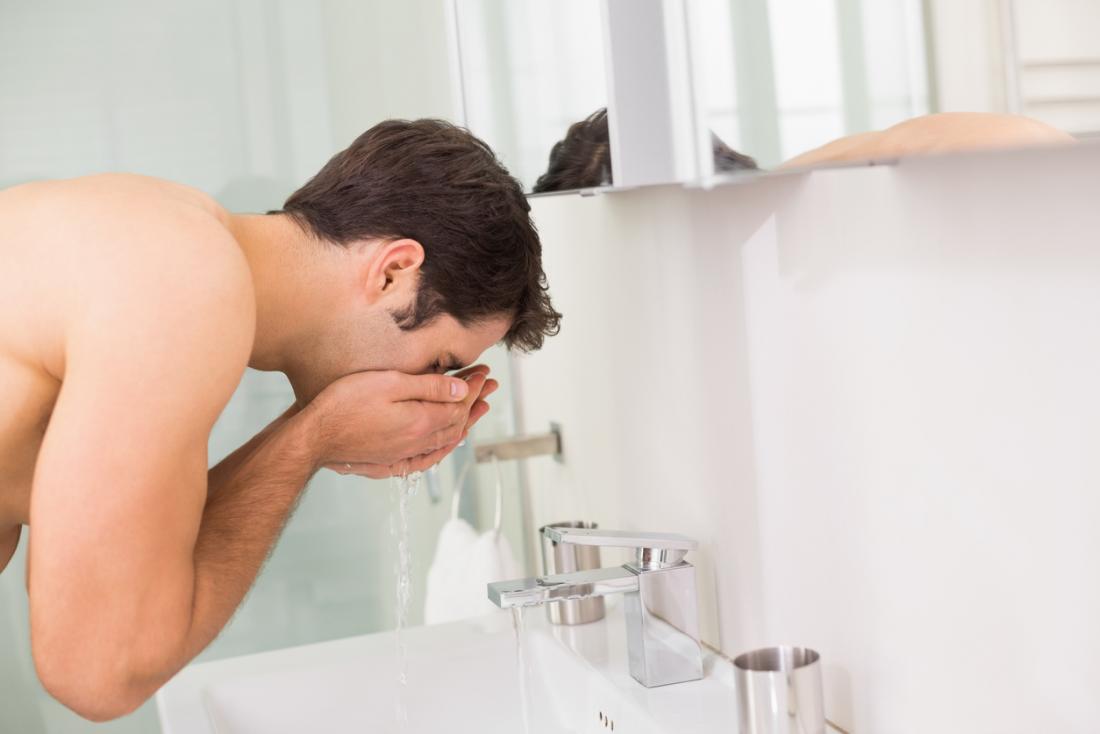 Man washing his face gently with water from bathroom sink.