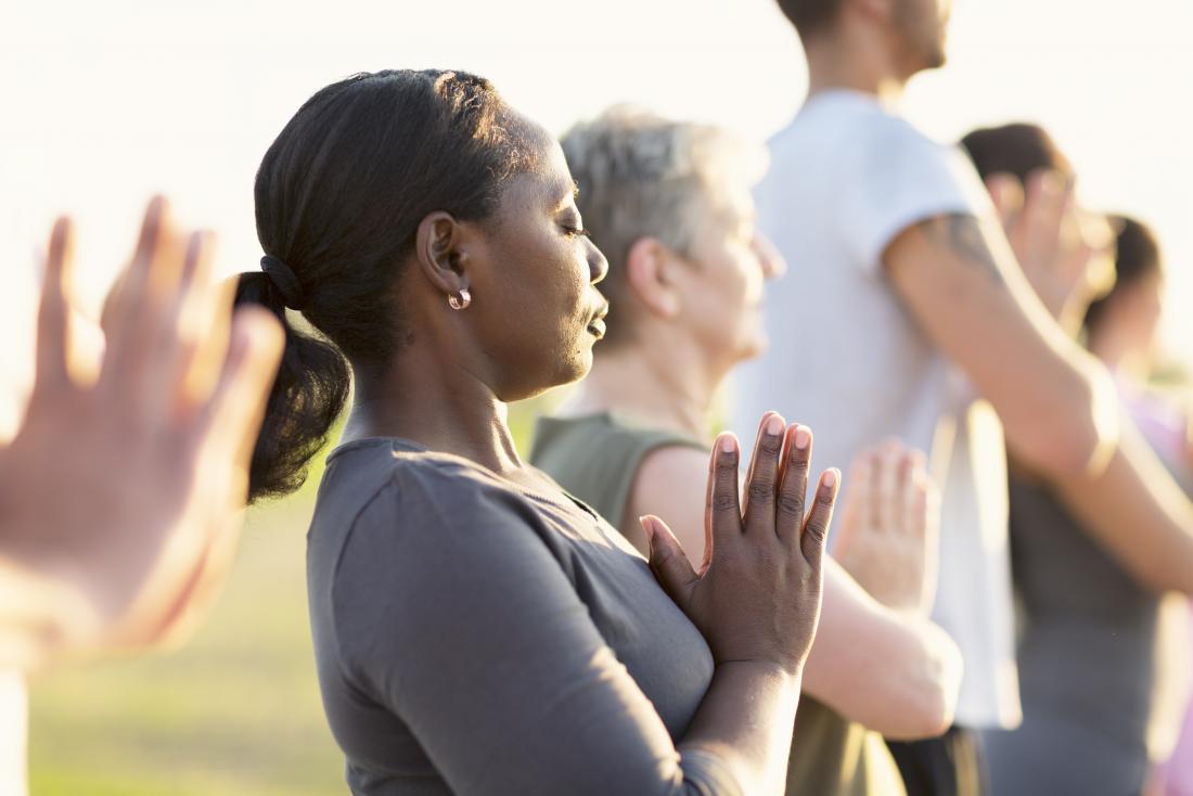 Woman practicing yoga and meditation outdoors with group.