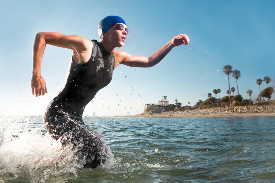 Muscular female swimmer competing in a triathlon, running out of sea.