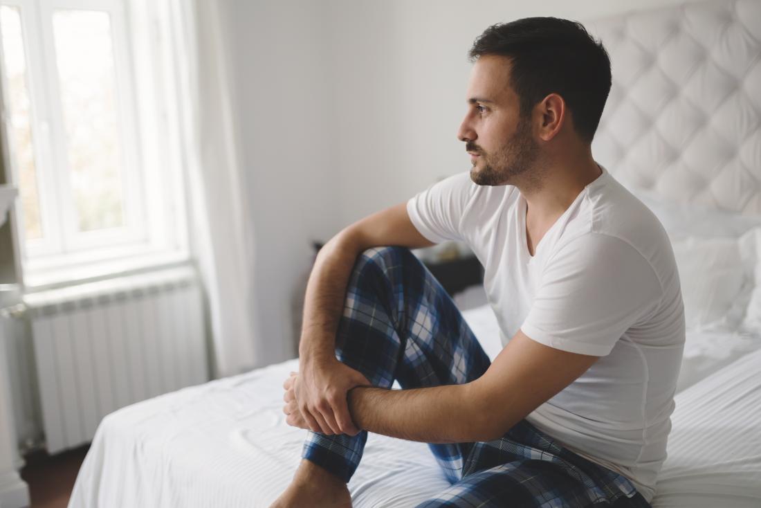 男人坐在床上看沉思，患有勃起功能障碍或ed。
