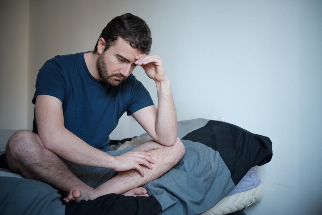 Depressed and anxious man sitting cross-legged on bed.