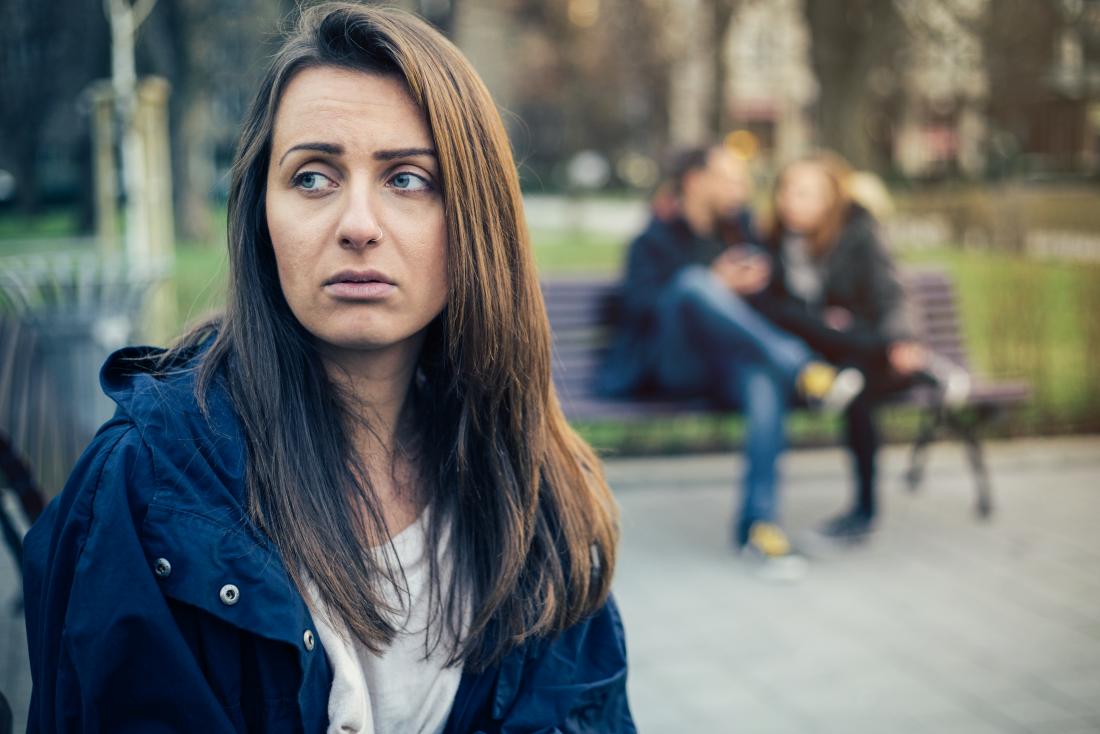 Sad woman sitting on her own while friends in the background sit together.