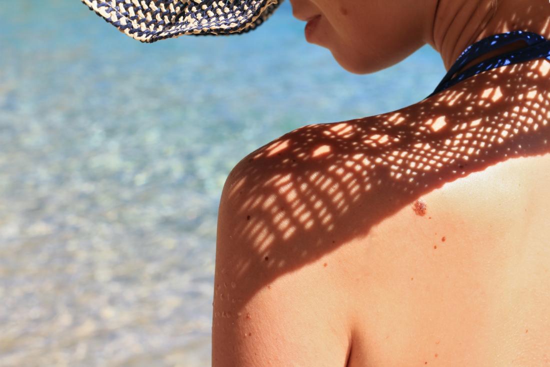Woman sunbathing by sea, wearing hat to protect skin.