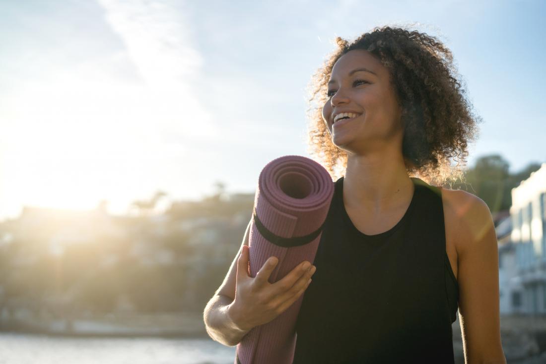 woman smiling outdoors with yoga mat in sunshine