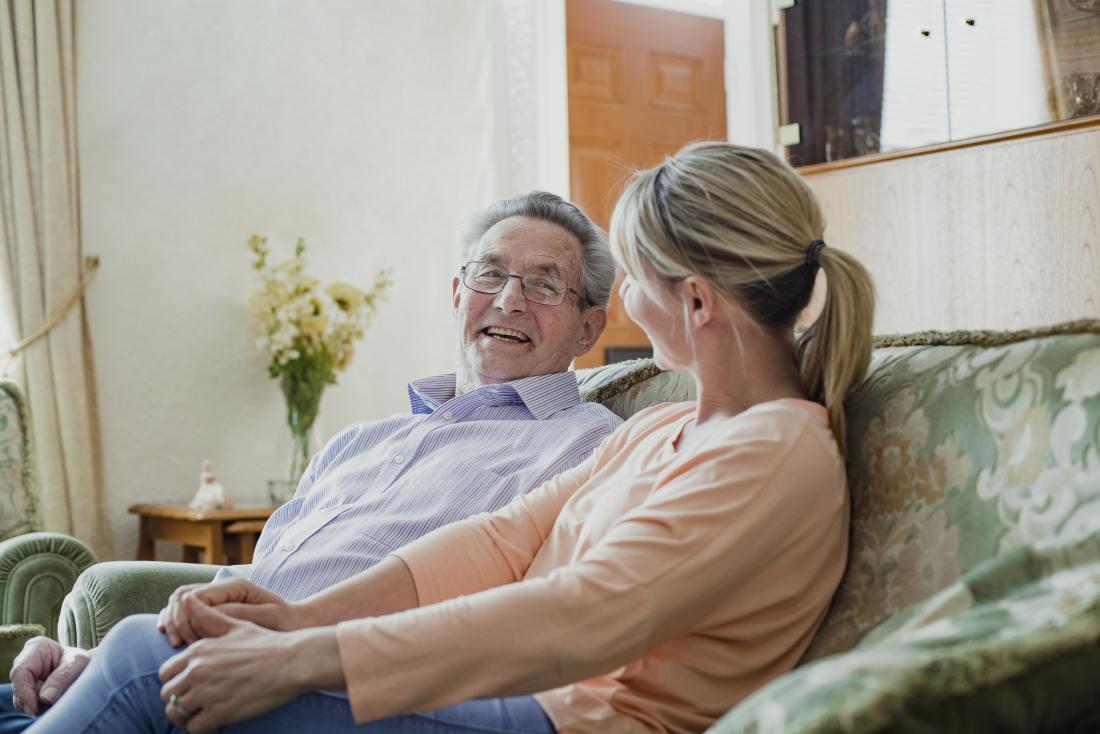 a woman and her elderly father share a laugh on the sofa.