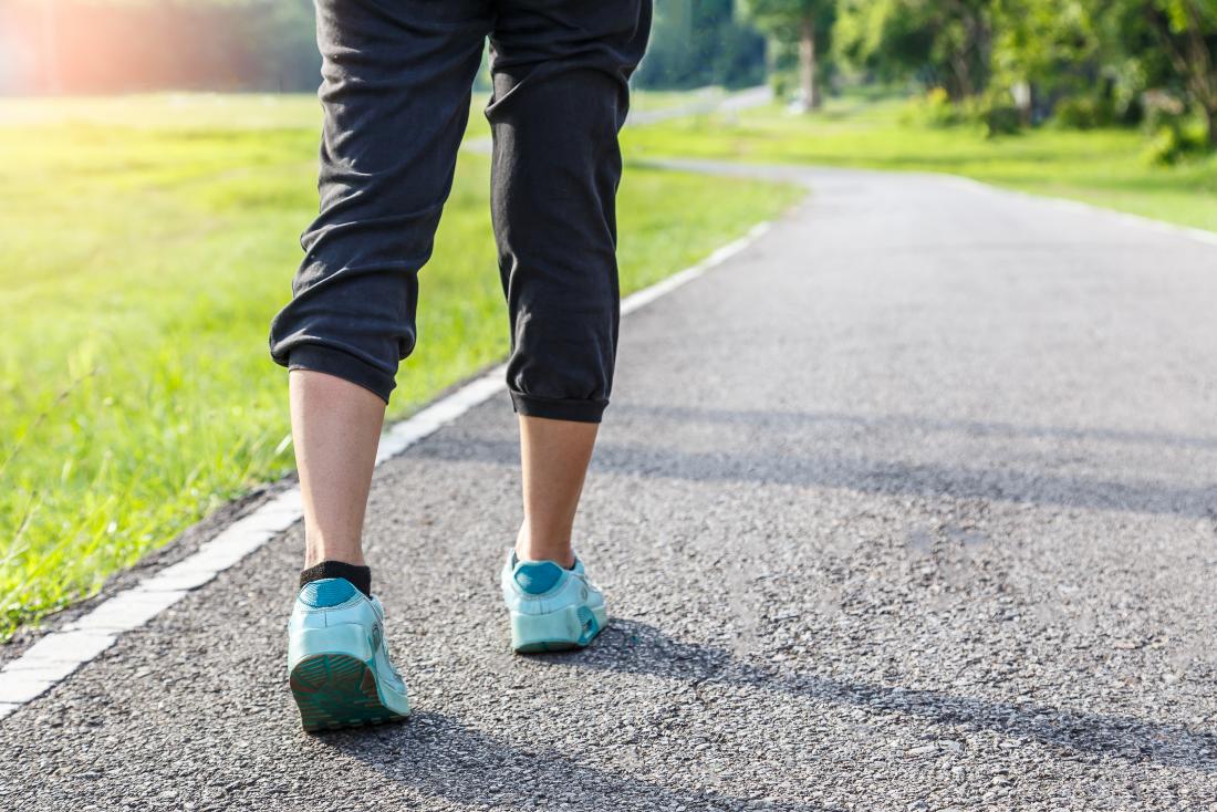 person walking with a steady gait around running track outdoors in sports clothes