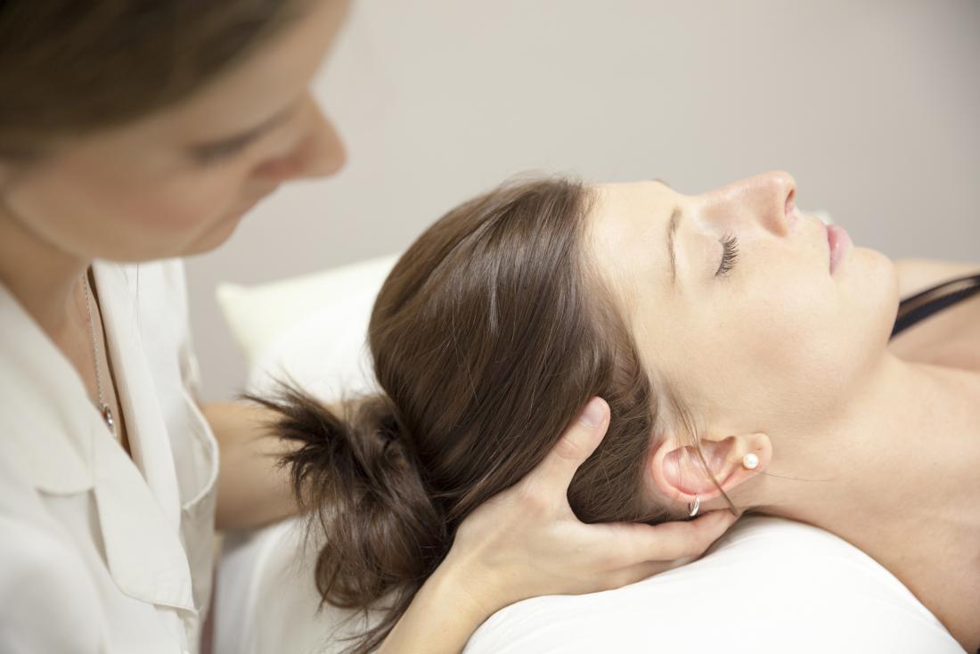 Chiropractor adjusting patient's head and neck on bed.