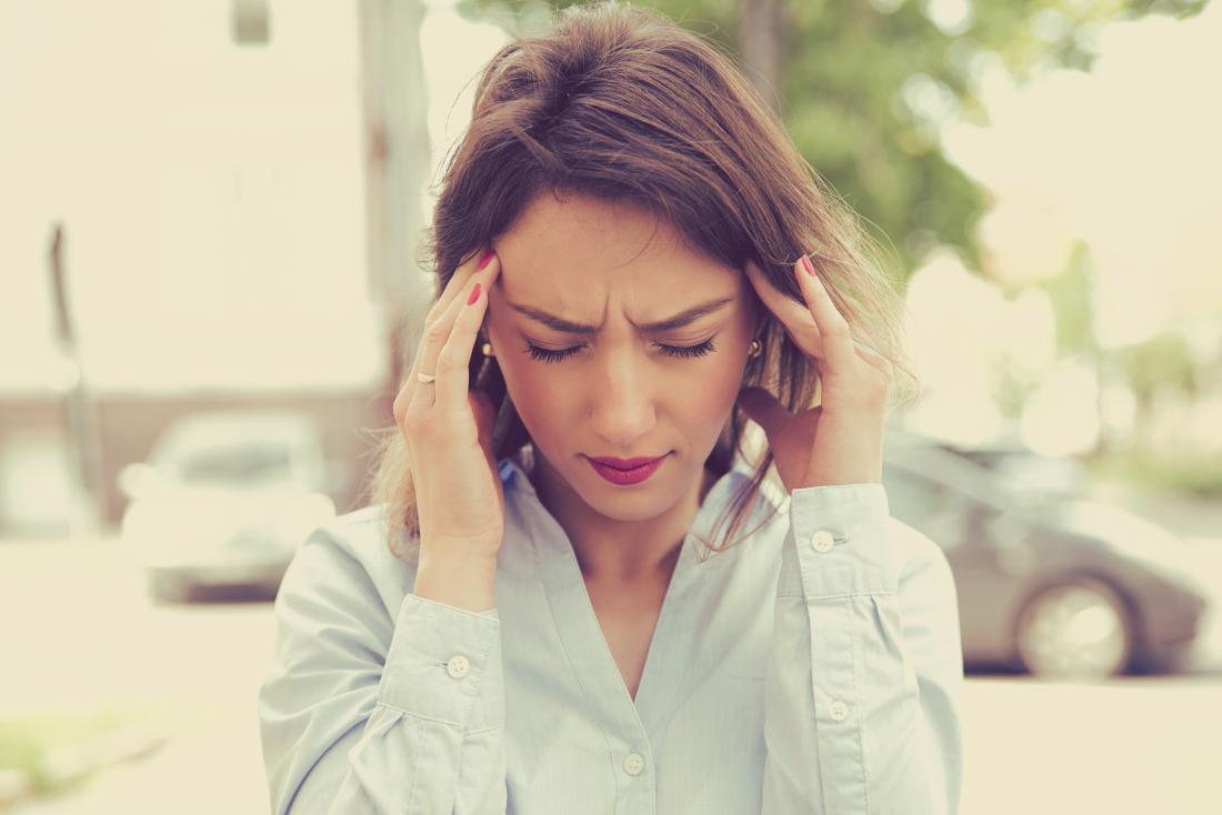 Woman with vertigo rubbing her temples and frowning because of headache pain, standing outside.