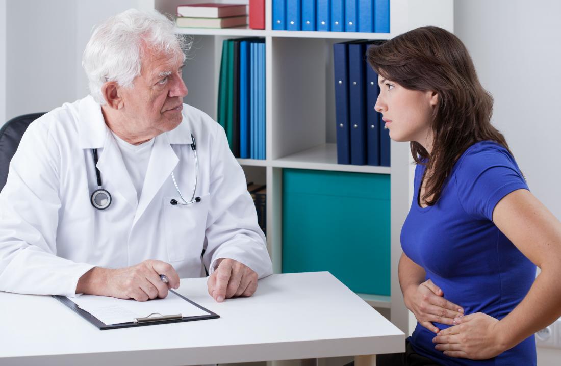 Woman with abdominal stomach pain speaking to doctor.