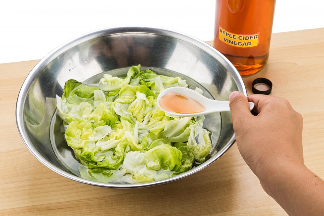 Person putting apple cider vinegar over salad leaves to soak.