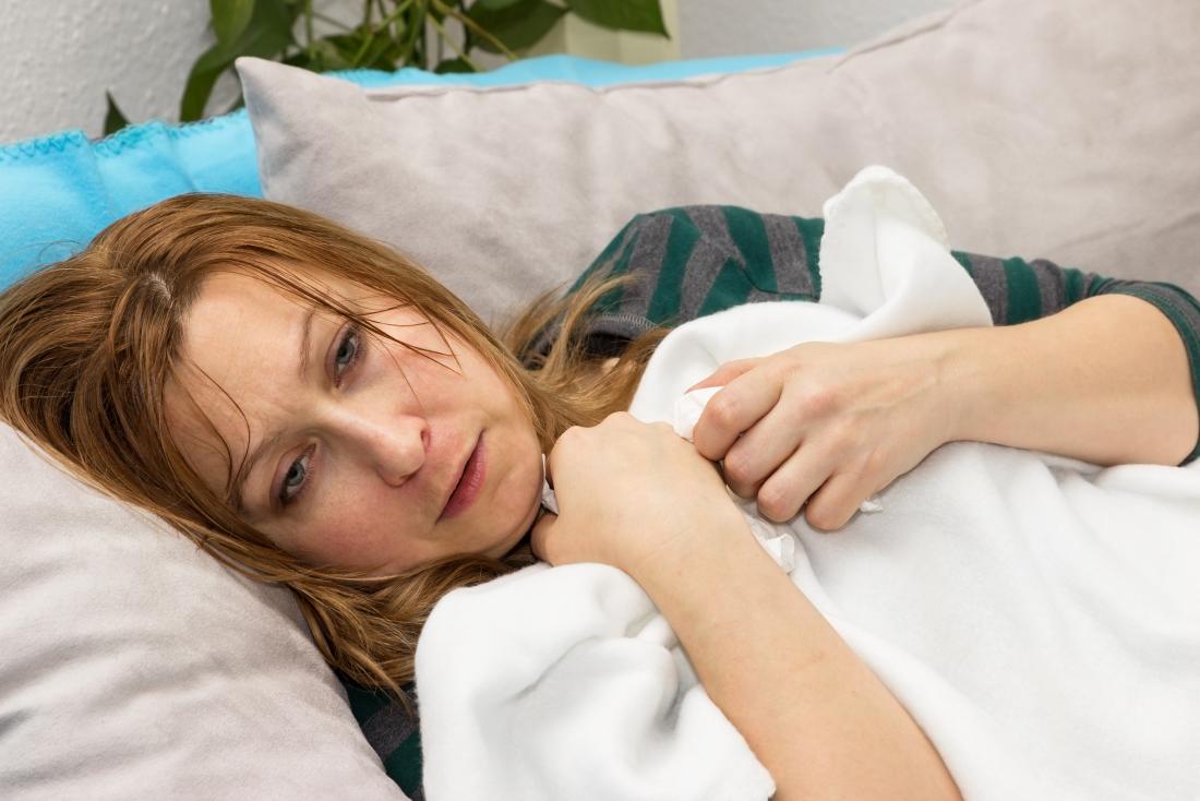 woman on sofa with blanket suffering from fever sweating and chills