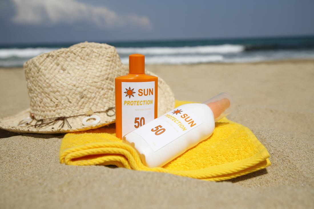 bottles of sun tan lotion towel and sunhat on the sand