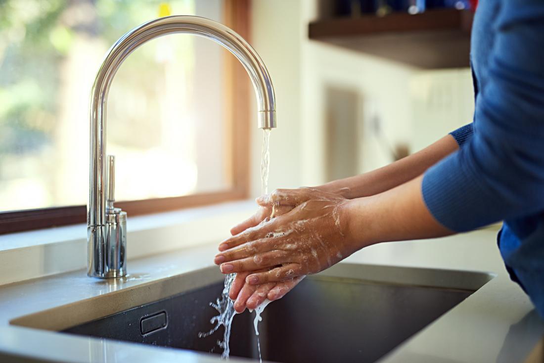 Person washing their hands in sink under running tap water.