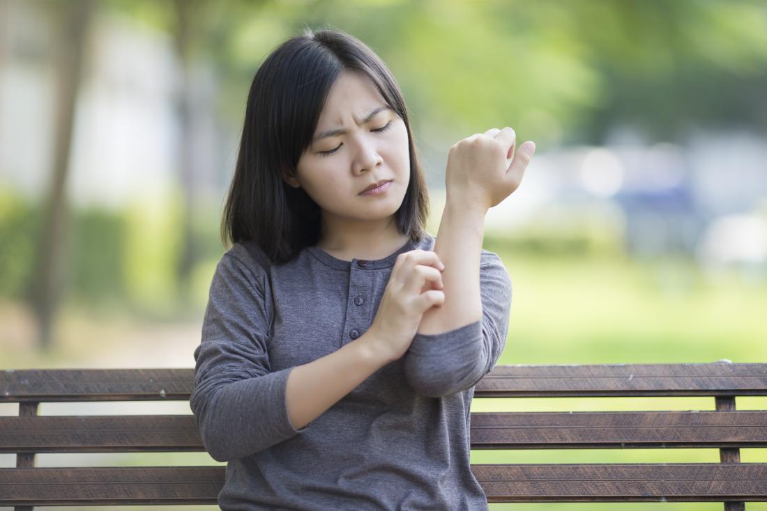 young woman sitting on a bench scratching her arm