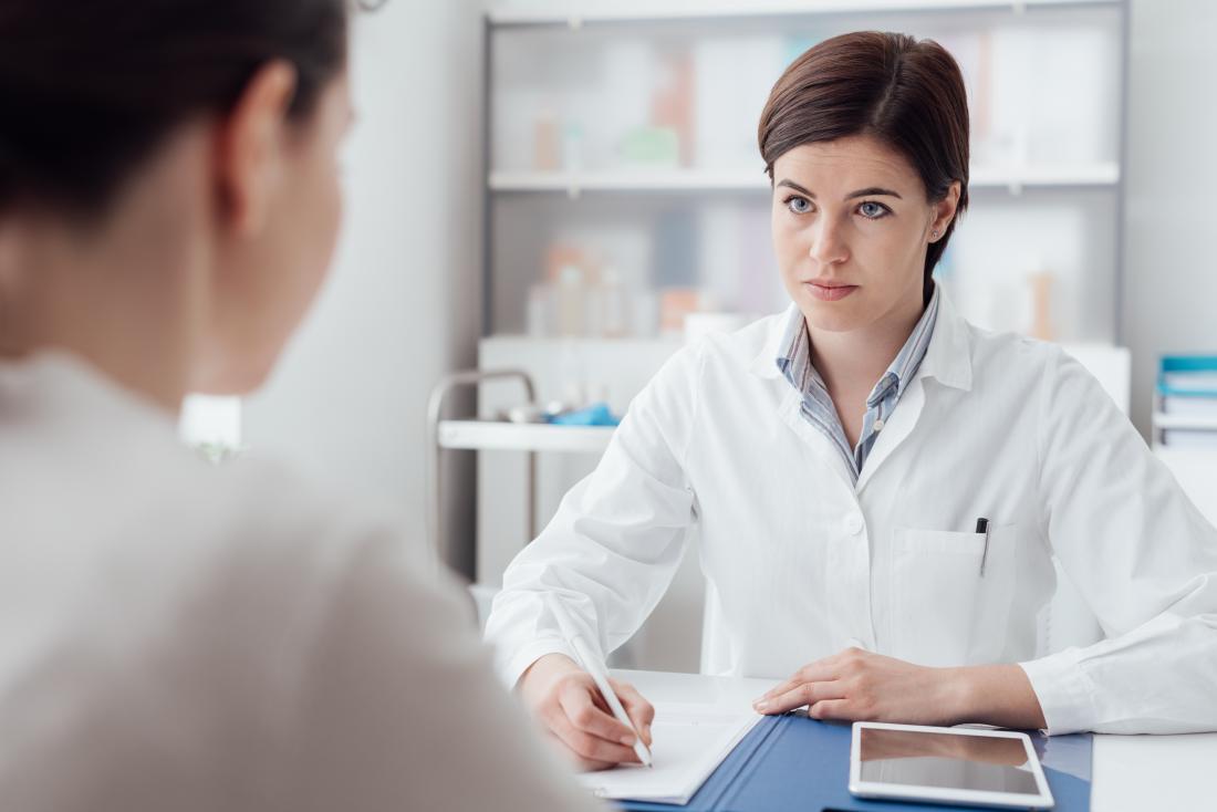 Doctor taking notes while listening to patient discuss medical problem.