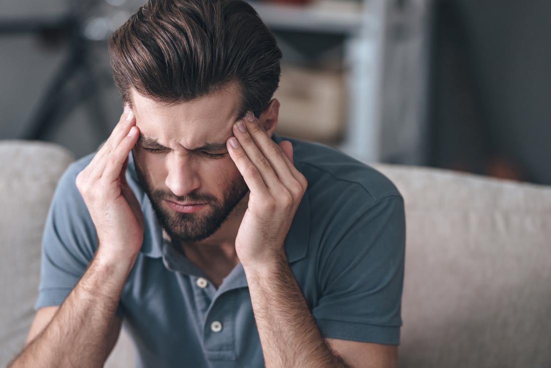 Man with migraine headache massaging his temples and frowning.