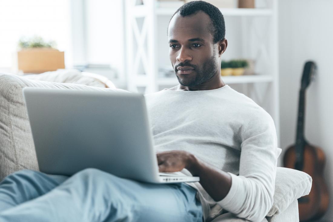 Man at home on couch, looking online with laptop.