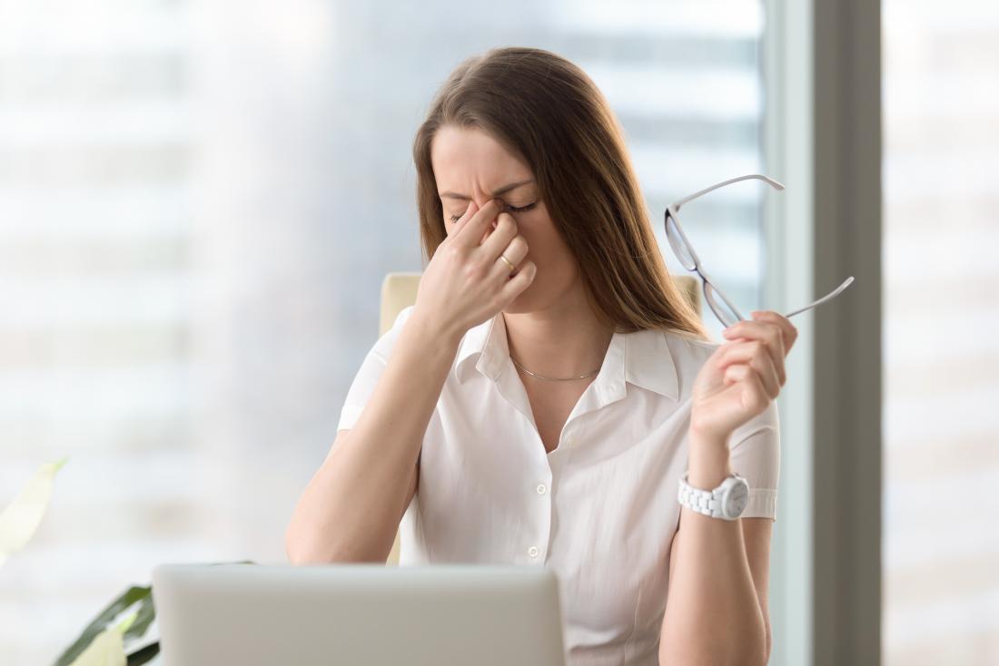 Woman at work holding eyes through stress. Possible risk factor for dyshidrotic eczema
