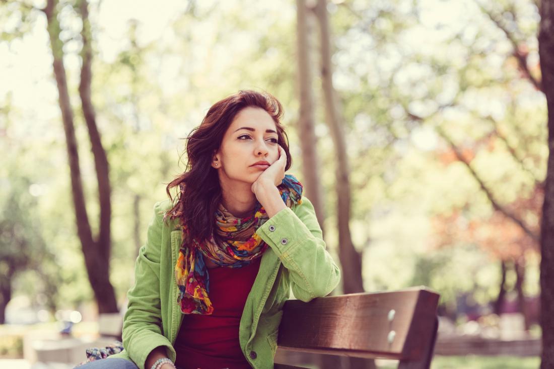 Woman sitting on park bench looking sad and contemplative.