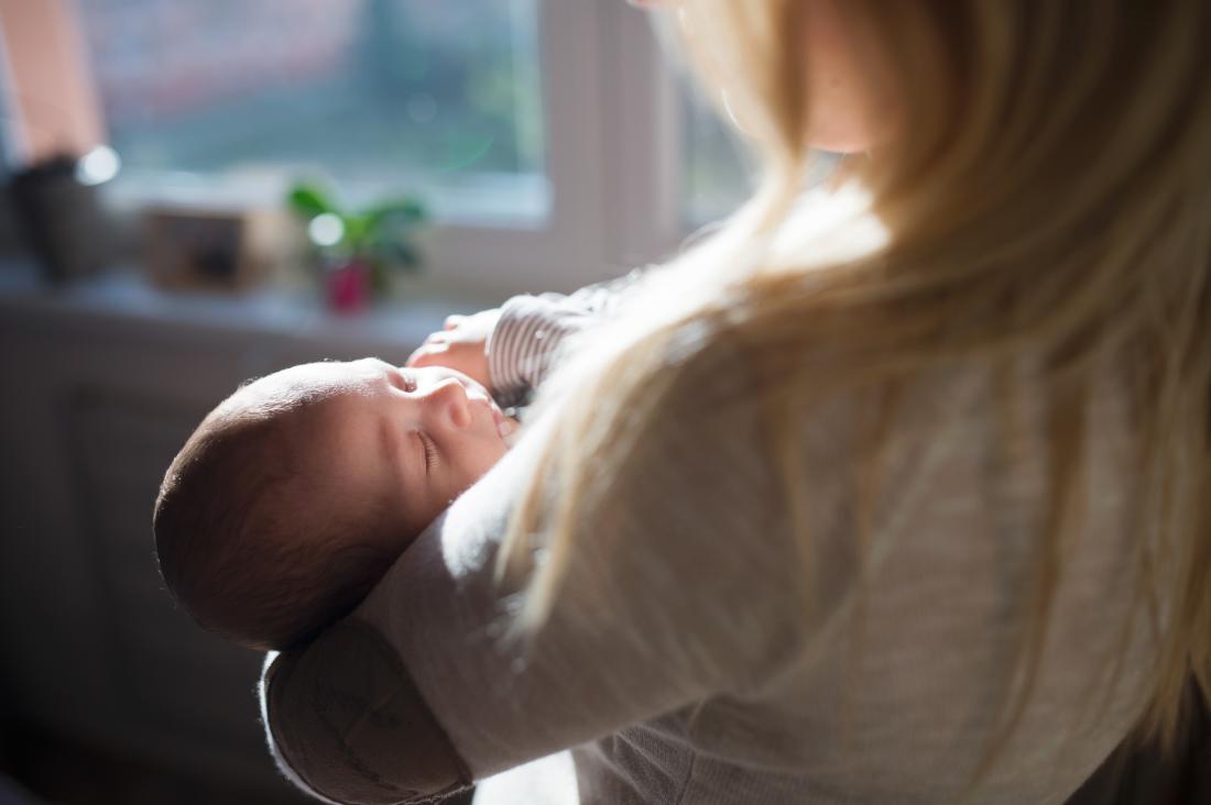 Hydranencephaly in baby's head highlighted by sunlight, held in woman's arms.