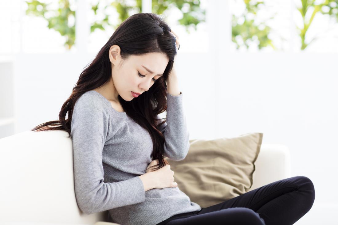 young woman sitting on settee holding stomach