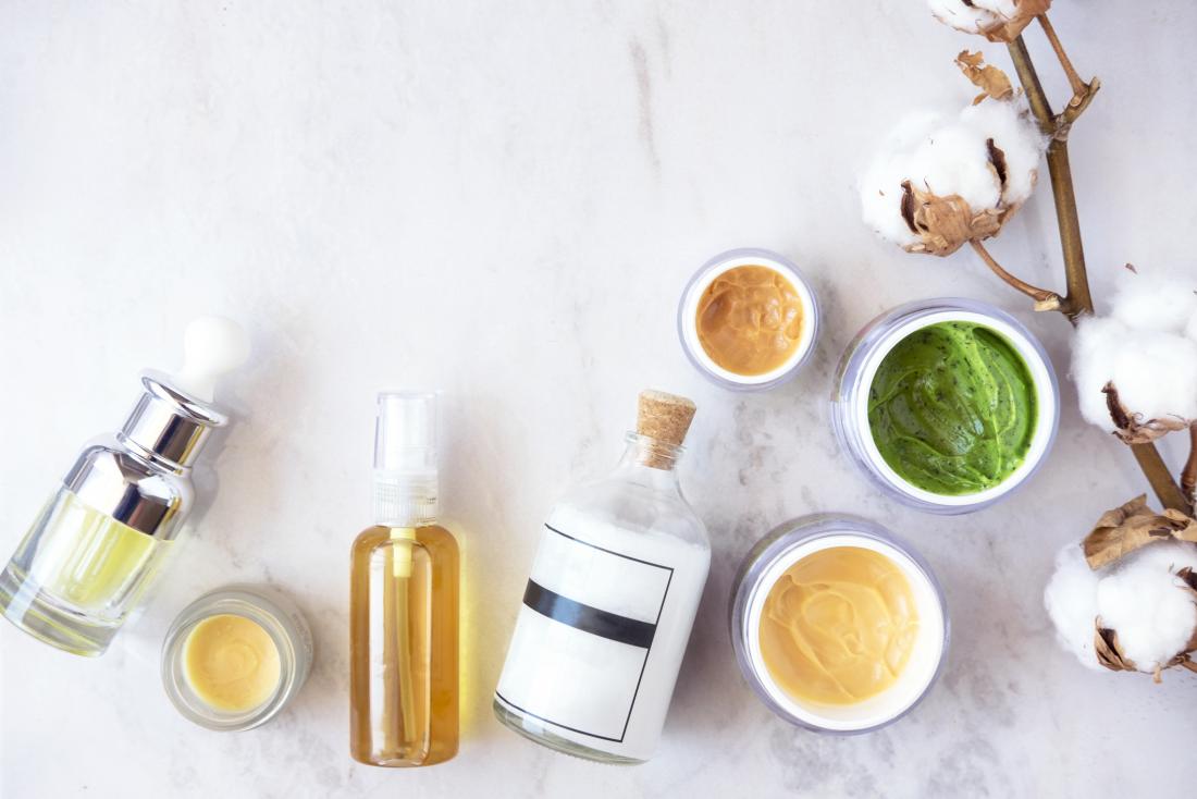 Different bottles, pots, and jars of skin lotion, body moisturizers, and oils on stone background.