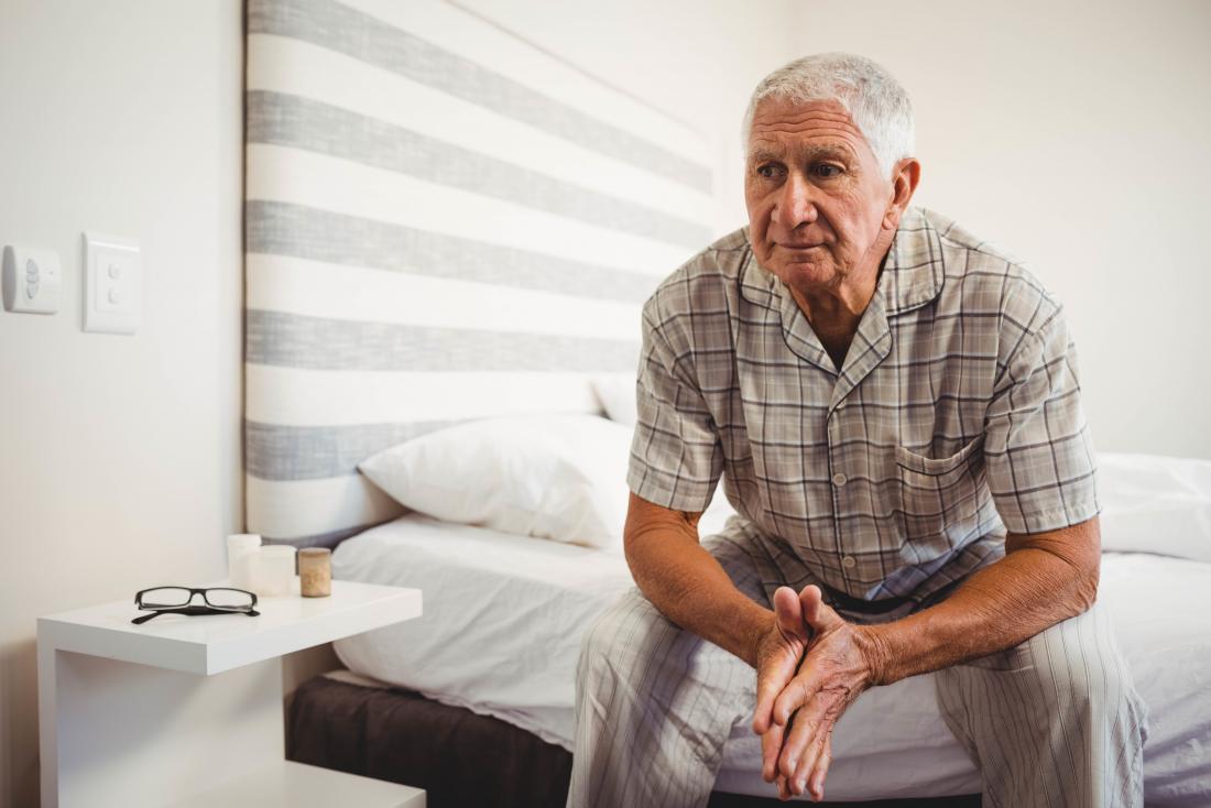 Older man sitting on edge of bed.