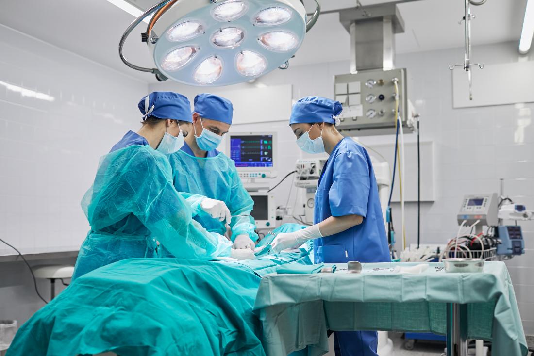 Surgeons around operating table in brightly lit theater.