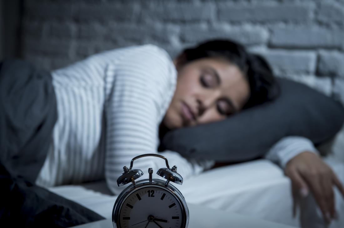 sleeping woman in bed with alarm clock in foreground