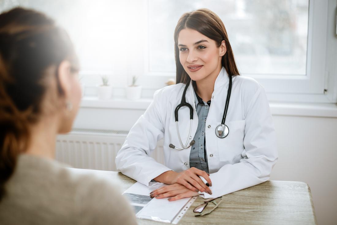 Doctor at desk listening to patient in foreground.