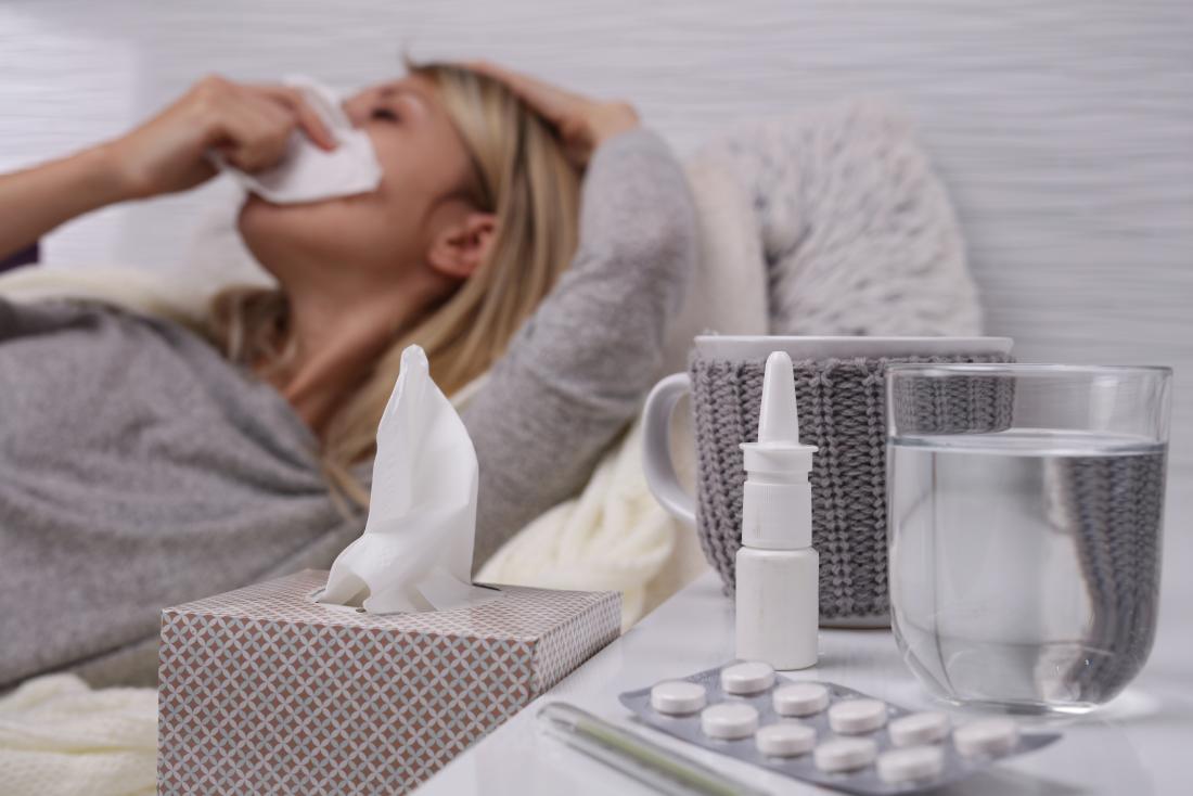 Woman suffering from cold and flu getting rid of phlegm and mucus using tissues, water, nasal spray, and medication.