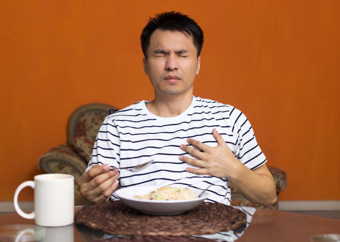 Man eating food suffering from acid reflux, touching chest in pain.