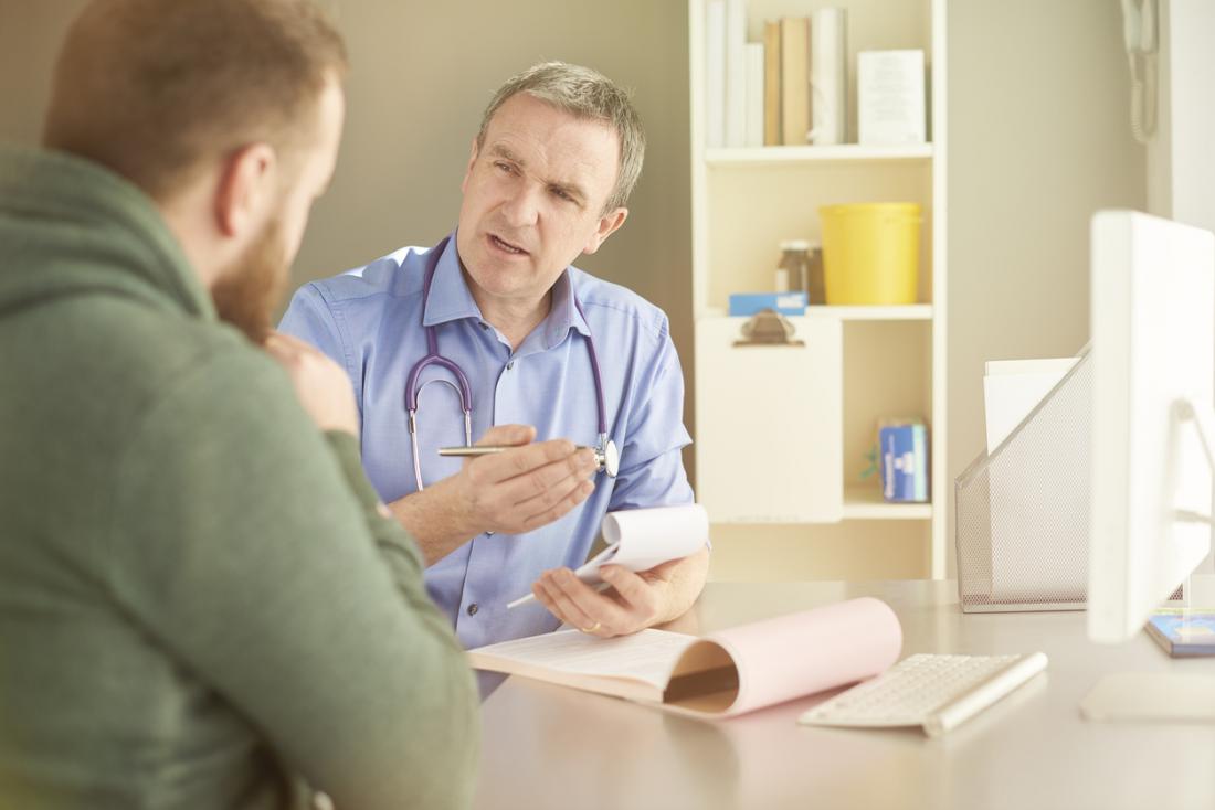 MAture male doctor with notepad explaining something to young male patient
