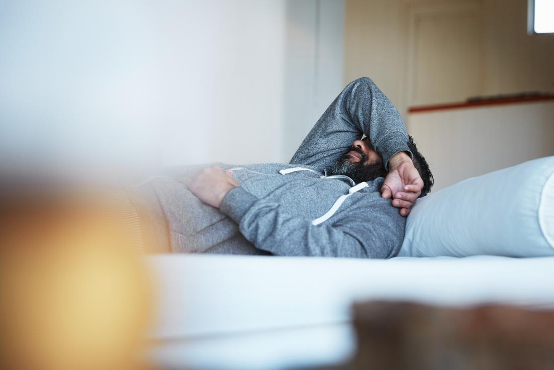 Hungover man lying on bed.