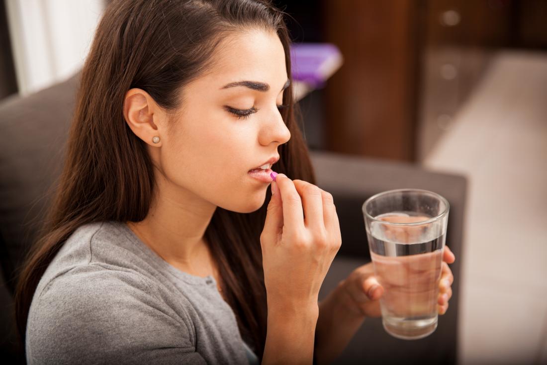 young woman taking a pill with a glass of water