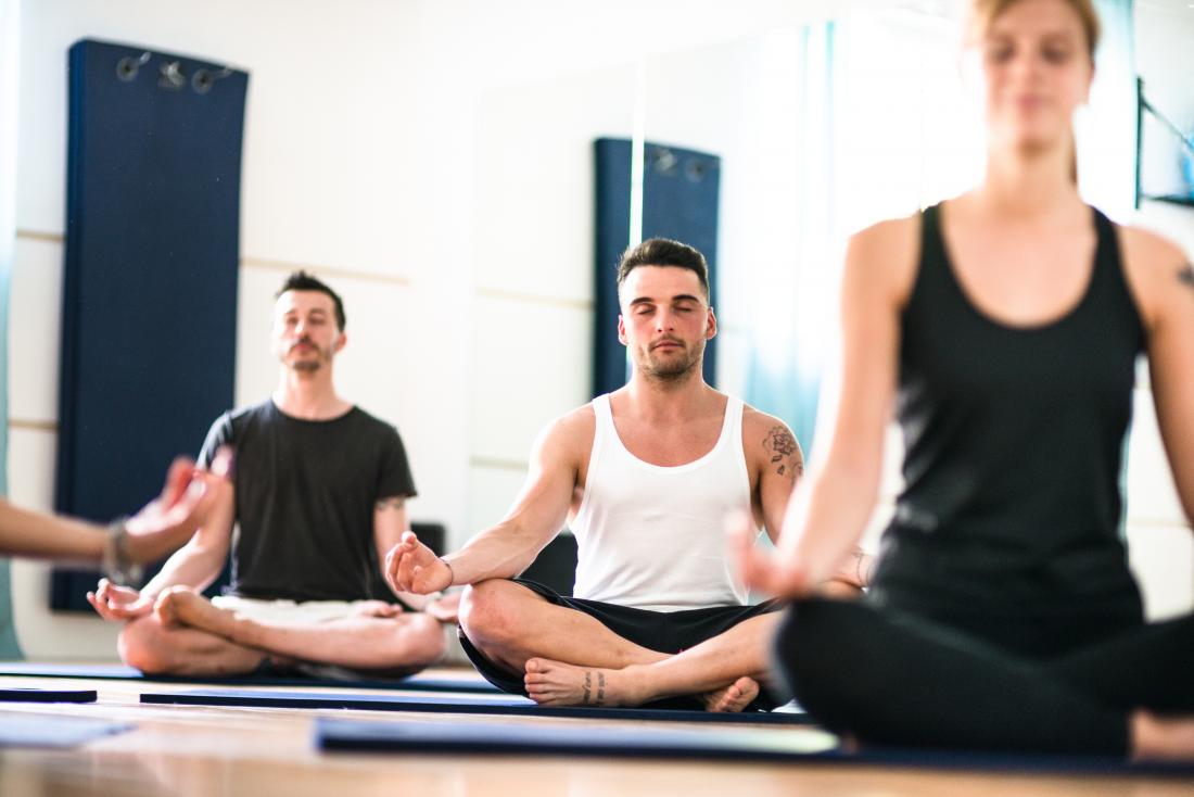 Yoga class in meditation pose, with man in middle on yoga mat.