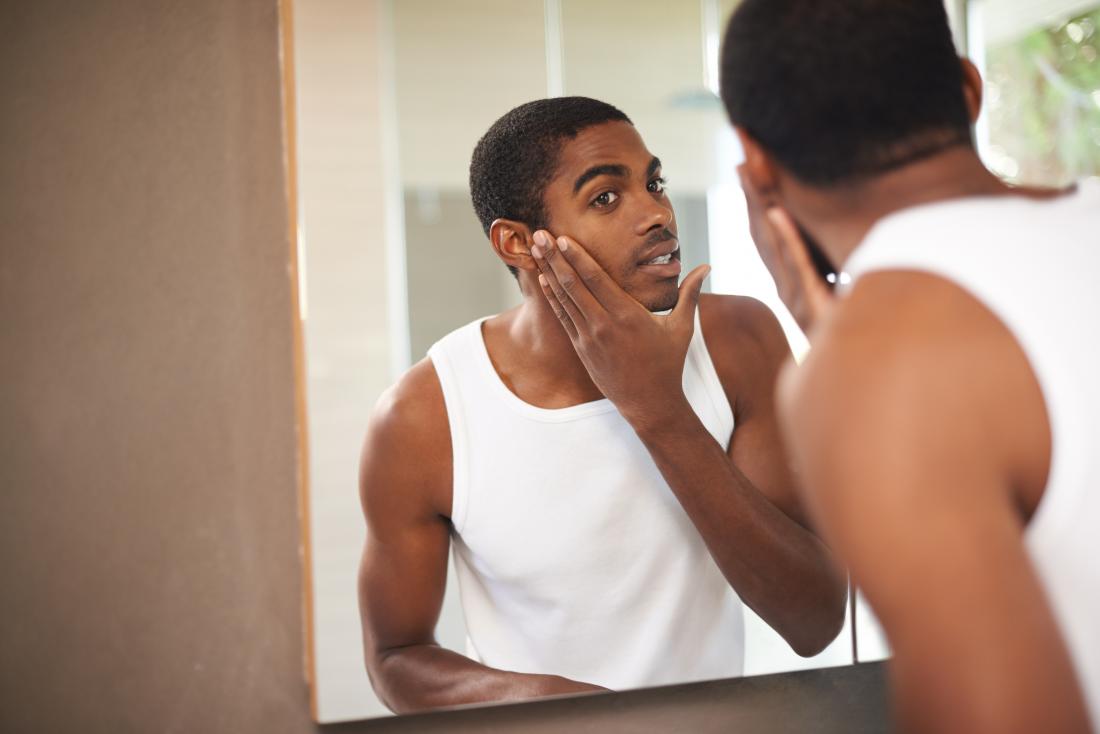 Man looking in mirror checking his face and putting product on.