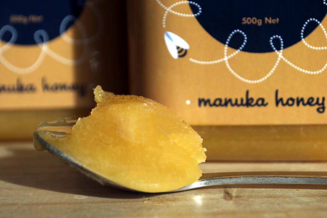 Manuka honey on spoon in front of pot.