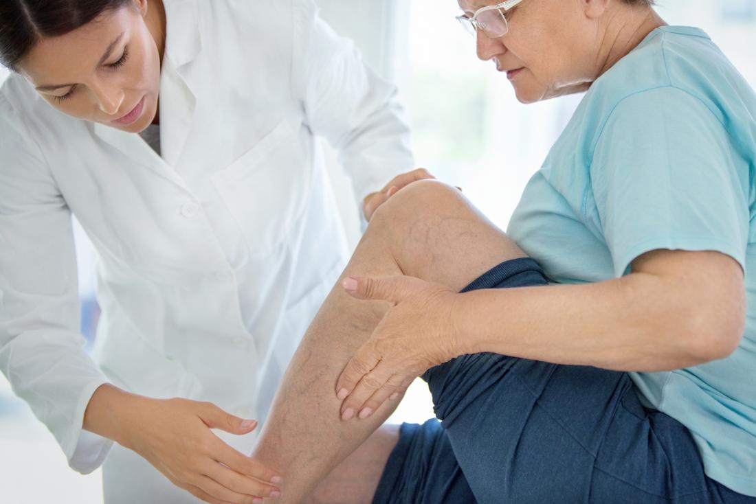 Calf pain in senior woman sitting on examination table with doctor.