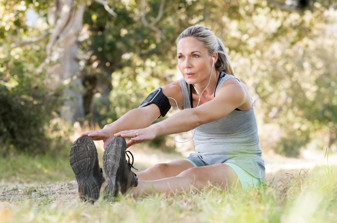 Woman sitting on ground outdoors touching toes performing foot flexion calf stretch