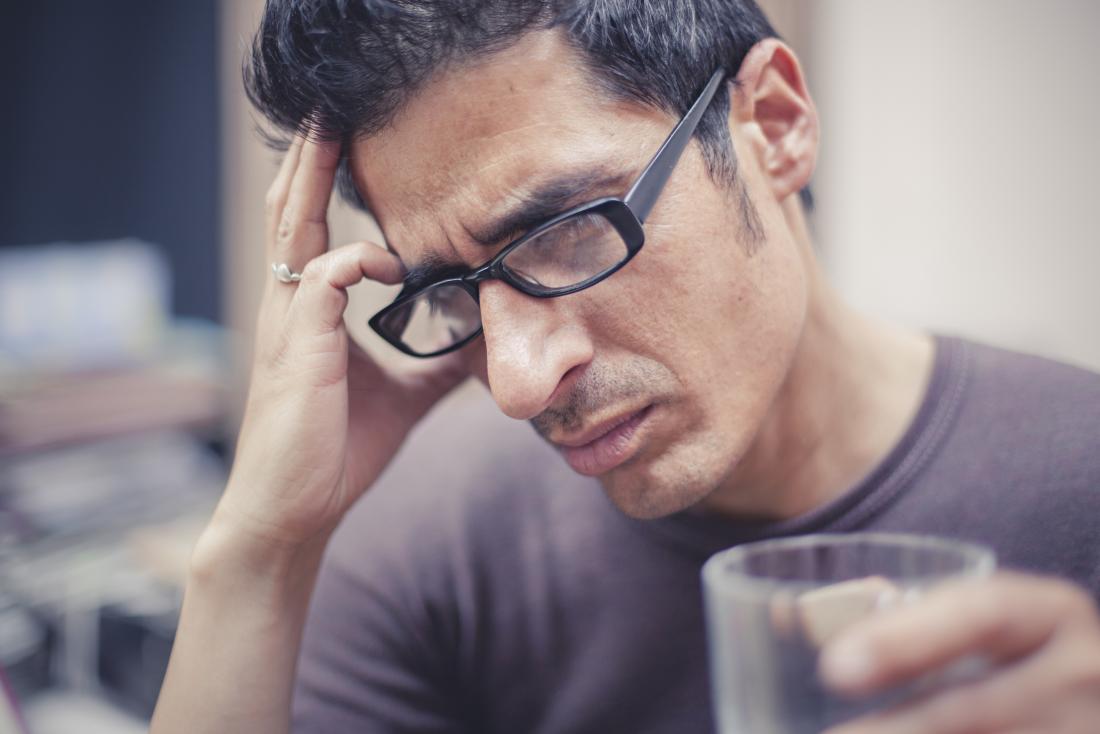 Man with headache on right side of head holding head and holding glass.